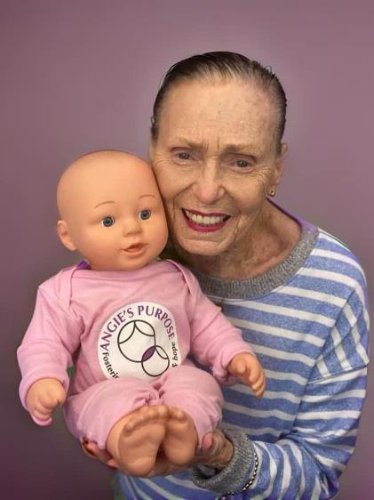 A woman smiling while holding a pink Angie’s Purpose doll against a purple background